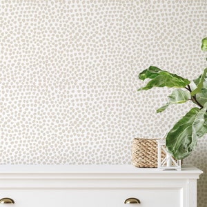 May include: Neutral-toned wallpaper with a speckled pattern, creating a subtle, textured backdrop. A white dresser with brass hardware and a woven basket add to the room's decor. A large potted plant with green leaves is on the right.