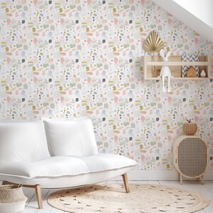 May include: White couch with two cushions in a room with a white wall covered in a colorful abstract pattern wallpaper. There is a small wooden shelf with a white rabbit figurine and a small house figurine on it. There is a small wooden side table with a woven basket on top and a woven rug on the floor.