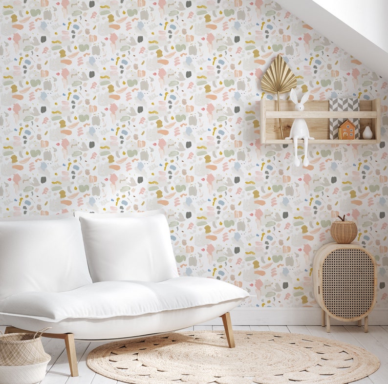 May include: White couch with two cushions in a room with a white wall covered in a colorful abstract pattern wallpaper. There is a small wooden shelf with a white rabbit figurine and a small house figurine on it. There is a small wooden side table with a woven basket on top and a woven rug on the floor.