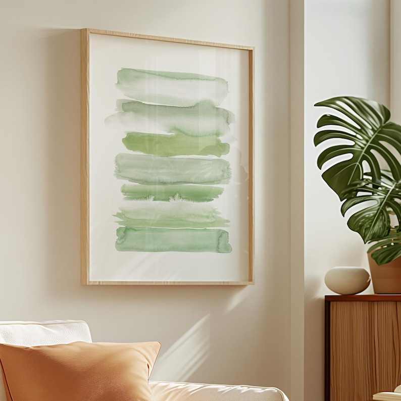 May include: A framed abstract watercolor painting with horizontal green brushstrokes on a white background. The frame is light wood.