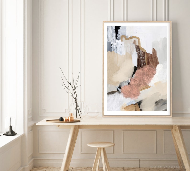 K&ouml;nnte beinhalten: Abstrakter Kunstdruck mit wei&szlig;em Hintergrund und braunen, beigefarbenen und rosafarbenen Farbschl&auml;gen. Der Druck ist in einem hellen Holzrahmen gerahmt und h&auml;ngt an einer wei&szlig;en Wand &uuml;ber einem Holztisch.
