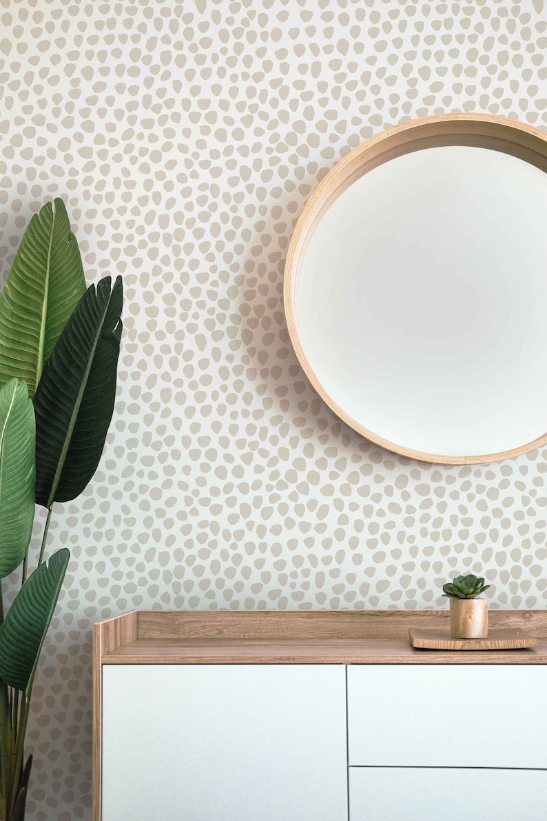 May include: A modern interior scene featuring a white cabinet with a wooden top, a round mirror with a wooden frame, and a potted plant. The wall is decorated with a beige pattern. A large green plant is on the left.