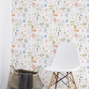 May include: A white chair with wooden legs sits in front of a wall covered in a colorful abstract wallpaper. The wallpaper features a repeating pattern of brushstrokes in shades of pink, blue, green, and yellow.