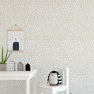 May include: A child's room with a white table, chair, and a wall with a beige dot pattern. A framed cat illustration hangs on the wall. A stuffed penguin sits on the chair. Decorative wooden houses and a plant are on the table.