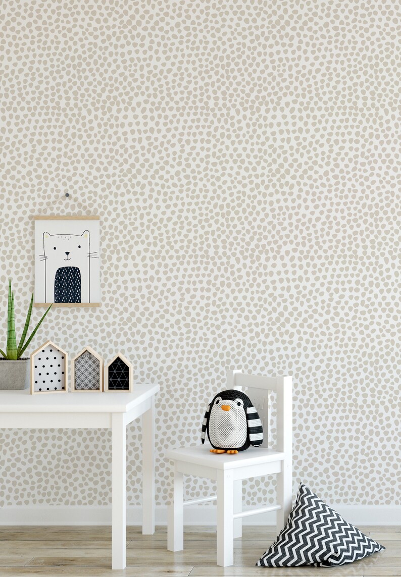 May include: A child's room with a white table, chair, and a wall with a beige dot pattern. A framed cat illustration hangs on the wall. A stuffed penguin sits on the chair. Decorative wooden houses and a plant are on the table.