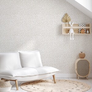 May include: A neutral-toned nursery or living room with a white sofa, a round jute rug, and a wooden cabinet. The walls are covered in a light beige dotted wallpaper. A small wooden shelf displays decorative items, including a gold leaf and a white bunny.