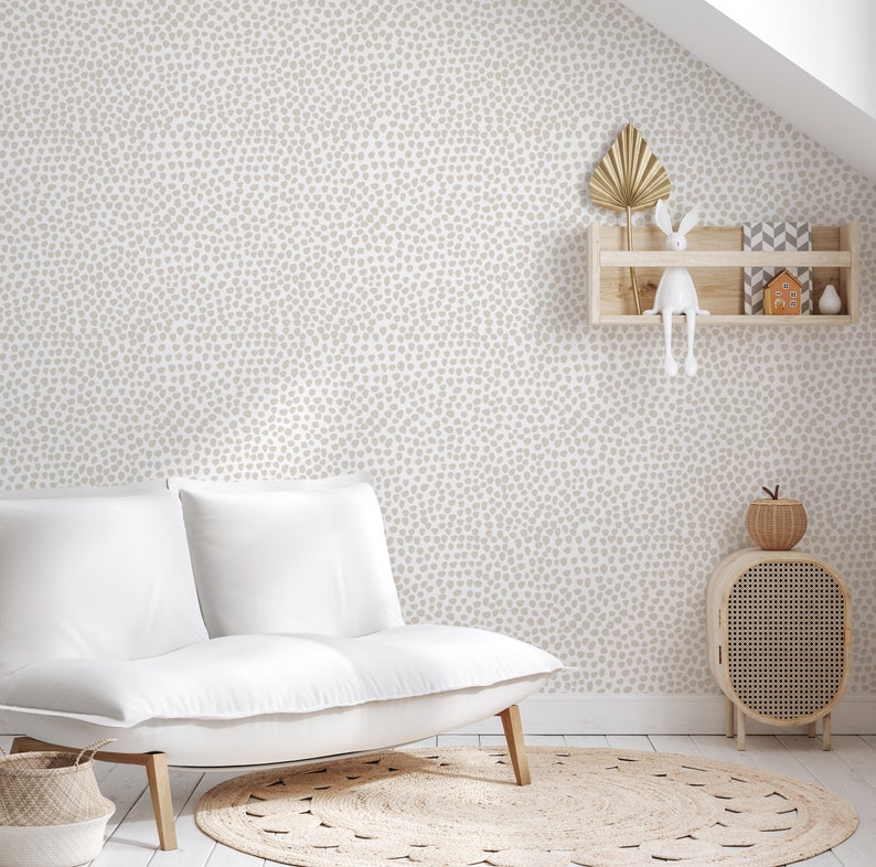 May include: A neutral-toned nursery or living room with a white sofa, a round jute rug, and a wooden cabinet. The walls are covered in a light beige dotted wallpaper. A small wooden shelf displays decorative items, including a gold leaf and a white bunny.