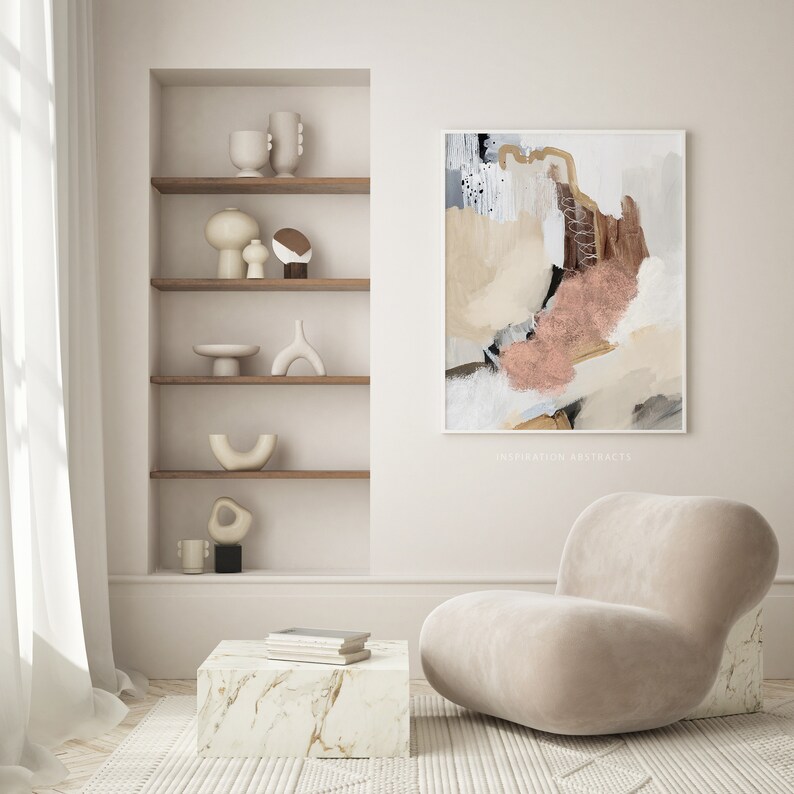 K&ouml;nnte beinhalten: Ein beiger Sessel mit abgerundeter R&uuml;ckenlehne und ein wei&szlig;er Marmor-Couchtisch mit einem Stapel B&uuml;cher darauf. Die Wand hinter dem Sessel zeigt ein gerahmtes abstraktes Gem&auml;lde in Beige-, Braun- und Rosat&ouml;nen. Der Text "inspiration artstracts" ist am unteren Rand des Gem&auml;ldes sichtbar.
