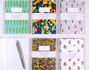 May include: Six small notebooks with different colourful patterns. The notebooks have a white label with the text "ALBAQUIRKY" and "Design for individuals" and "3 notebooks".