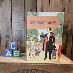 Könnte beinhalten: Ein altes Kinderbuch mit dem Titel "Surprises For Us" mit einer bunten Illustration eines Magiers, der einen Hasen aus einem Hut zieht. Das Buch liegt auf einer Holzkiste mit dem aufgedruckten Text "Cal-Pac From The Land Of Sunshine".