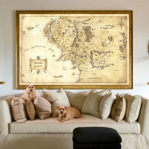 May include: A framed map of Middle Earth hangs above a cream-colored sofa with several pillows. The map is in sepia tones with intricate details. Two small dogs are on the sofa. Decorative side tables and wall sconces flank the sofa.