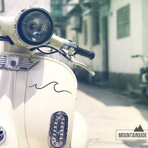 Puede incluir: Un scooter vintage blanco con una calcoman&iacute;a de onda negra en el lateral. El scooter est&aacute; estacionado en un callej&oacute;n estrecho con un edificio en el fondo. El scooter tiene un faro cromado y un manillar cromado.