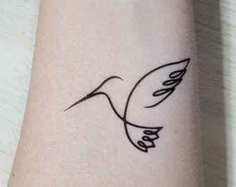 May include: A simple line drawing tattoo of a hummingbird on a person's arm.
