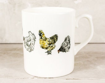 May include: A white ceramic mug featuring a series of detailed illustrations of three chickens. The artwork depicts a fluffy white chicken, a golden-brown speckled chicken, and a smaller dark grey chicken, all rendered in a realistic artistic style.