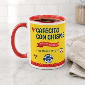 May include: A ceramic mug with a bright yellow exterior and a red handle and rim. The front features the text "CAFECITO CON CHISME" in blue, "Edición Especial" on a red banner, "100% FRESH GOSSIP", and a blue "CERTIFIED CHISME ANALYST" seal.