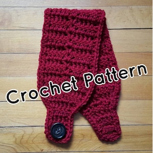 Puede incluir: Una diadema de ganchillo roja, hecha a mano, con cierre de botón. La diadema está hecha de un hilo grueso y texturizado y presenta el texto "Crochet Pattern" en letras blancas.