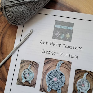 May include: A crochet pattern for cat butt coasters. The pattern includes instructions and images of the finished product. The coasters are gray with a pink center and a tail.