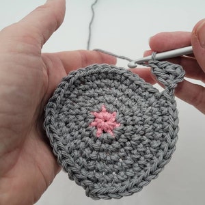 May include: A gray crocheted circle with a pink crocheted star in the center.
