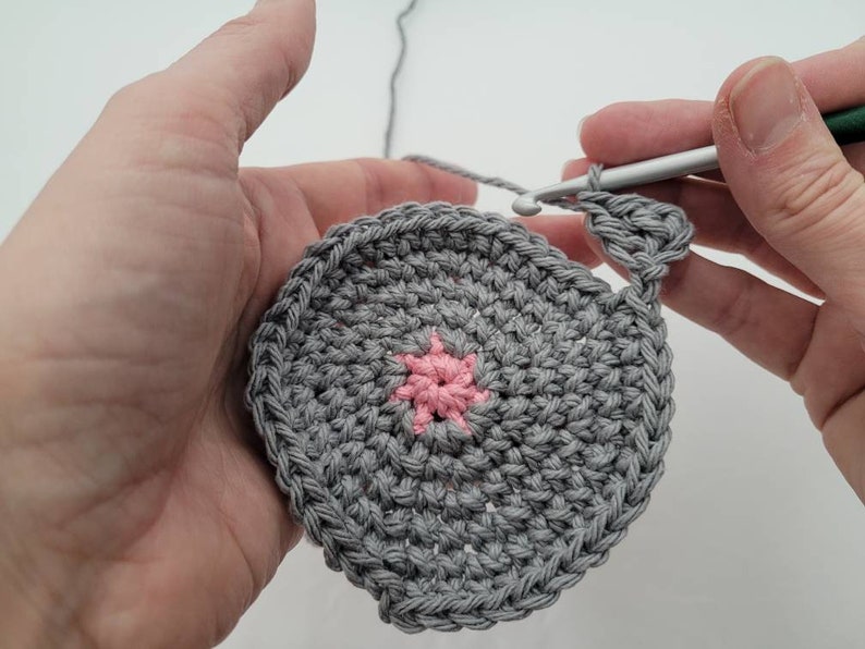 May include: A gray crocheted circle with a pink crocheted star in the center.