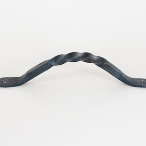 Peut inclure: Une poignée en fer forgé noir avec un design torsadé. La poignée est incurvée avec des plaques de montage plates à chaque extrémité, chacune avec un seul trou pour les vis. Le métal a une finition mate texturée.