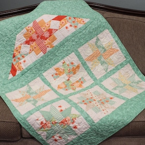 May include: A mint green quilt with a patchwork design featuring various floral and geometric patterns in shades of pink, orange, and white.