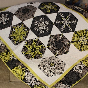 May include: A handmade quilt with a geometric pattern. The quilt features black, white, and gray hexagonal shapes with floral designs, accented by lime green and a white background. The border has a floral pattern with a lime green trim.