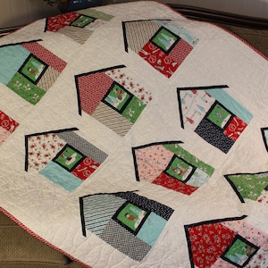 May include: A white quilt with a red, white, and blue border. The quilt is made up of 10 squares, each with a different pattern of houses. The houses are all different colors and have different designs.