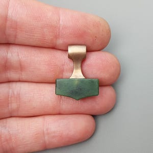 Hand holding a bronze Mjolnir pendant carved from natural nephrite jade.