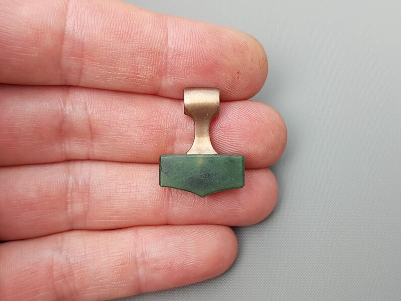 Hand holding a bronze Mjolnir pendant carved from natural nephrite jade.