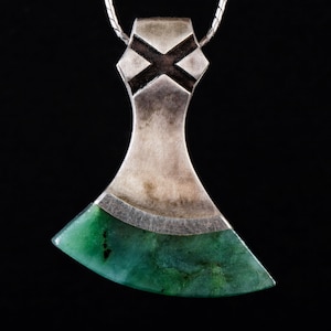 May include: A silver axe pendant with a green stone inlay. The axe head is detailed with a black cross design.