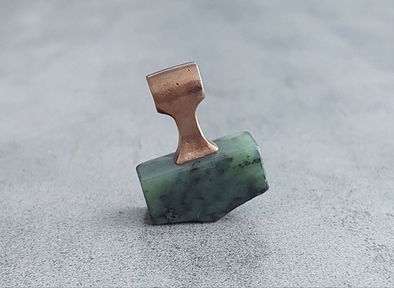 May include: A green stone pendant with a copper-colored bail. The stone is irregularly shaped and has a rough texture.