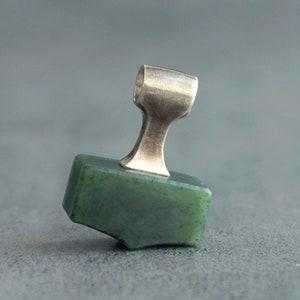 May include: A green jade stone pendant with a silver bail. The pendant is shaped like a small hammer.