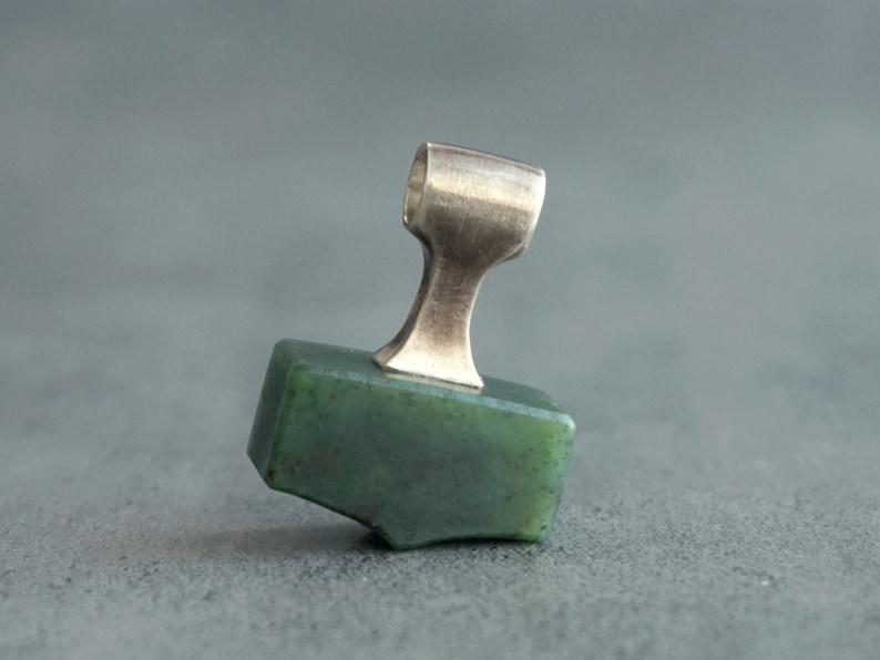 May include: A green jade stone pendant with a silver bail. The pendant is shaped like a small hammer.