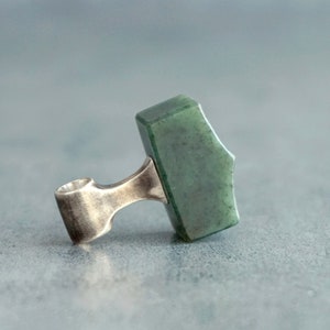 May include: A silver pendant with a green jade stone shaped like a hammer.
