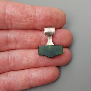 Hand holding a silver Mjolnir pendant with natural nephrite jade.