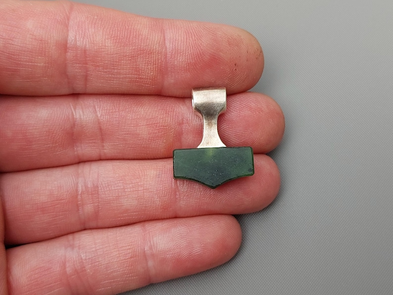 Hand holding a silver Mjolnir pendant with natural nephrite jade.