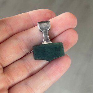May include: A silver and green Mjolnir pendant, a Norse symbol of Thor's hammer.