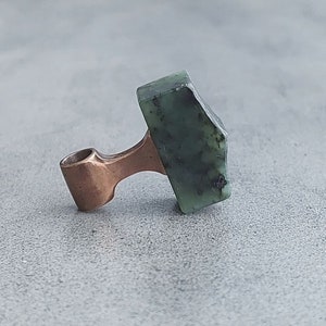 May include: A copper pendant with a green stone in the shape of a hammer.