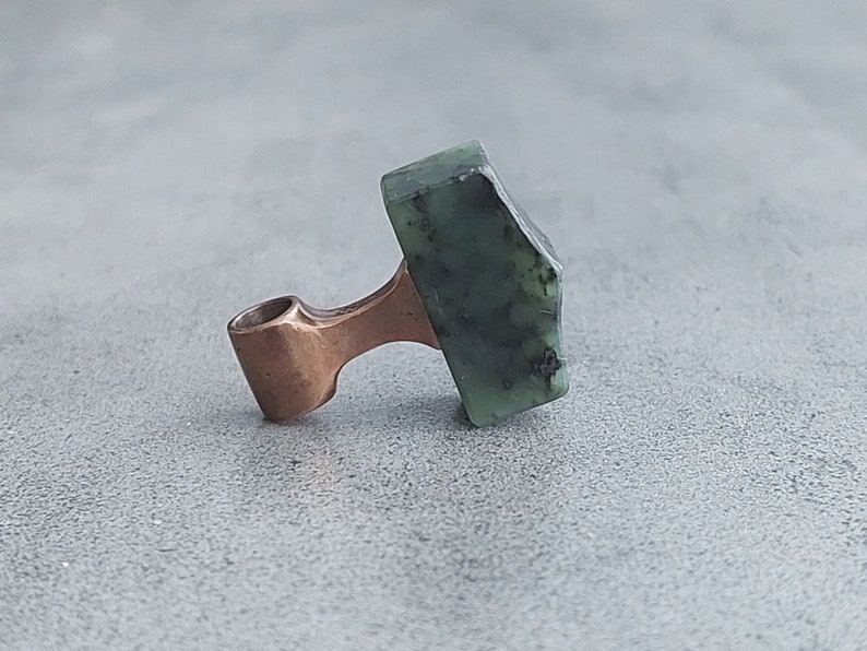 May include: A copper pendant with a green stone in the shape of a hammer.