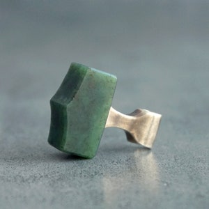 May include: A green stone hammer pendant with a silver metal loop. The stone is a deep green color with a slightly textured surface.