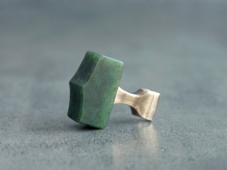 May include: A green stone hammer pendant with a silver metal loop. The stone is a deep green color with a slightly textured surface.