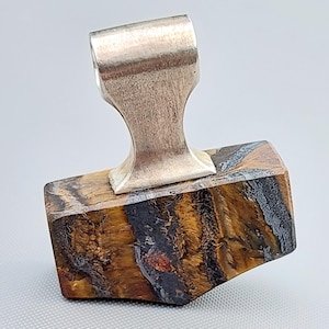 May include: A pendant featuring a rectangular piece of tiger's eye gemstone with brown, gold, and dark grey bands. A polished silver-toned metal bail is attached to the top centre of the stone, providing a loop for a chain or cord to pass through.