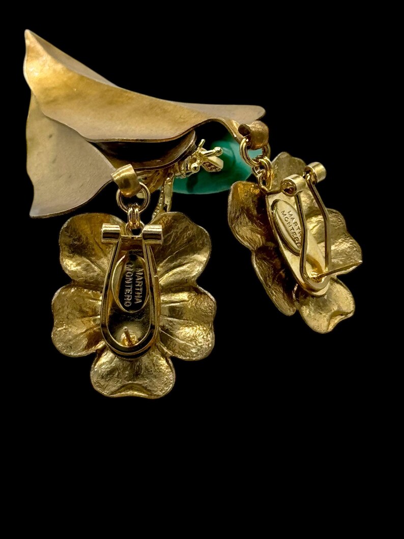 May include: Gold tone flower-shaped earrings with a green stone and a Martha Monteiro tag on the back.
