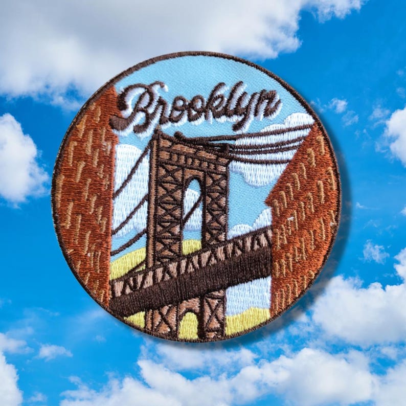 May include: A round embroidered patch with a brown bridge, blue sky, and white clouds. The text "Brooklyn" is embroidered in white on a blue background.