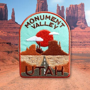 May include: A red, white, and brown embroidered patch with the text "Monument Valley Utah" and a depiction of a desert landscape with a red sun and a road.