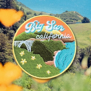 May include: A round embroidered patch with a sunset orange background and the text "Big Sur California". The patch features a green and brown landscape with a bridge and a blue ocean.