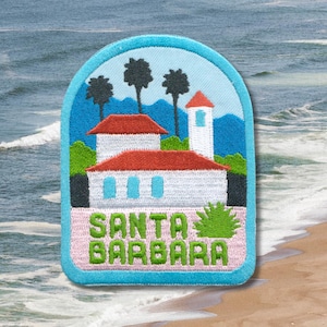 May include: Embroidered patch featuring a Santa Barbara scene. The design includes white buildings with red roofs, palm trees, and the text "SANTA BARBARA" in green. The patch has a light blue border and a pink base.