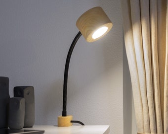 May include: A wooden desk lamp with a black flexible arm and a white light bulb. The lamp is on a white desk with a laptop and other objects.