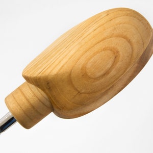 May include: A wooden bottle stopper with a rounded, oval-shaped top. The stopper is made of light brown wood with visible grain patterns.