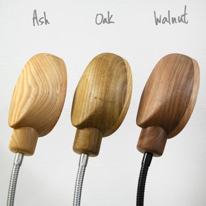 May include: Three table lamps with different wood finishes: ash, oak, and walnut. Each lamp has a flexible metal arm and a round wooden shade.